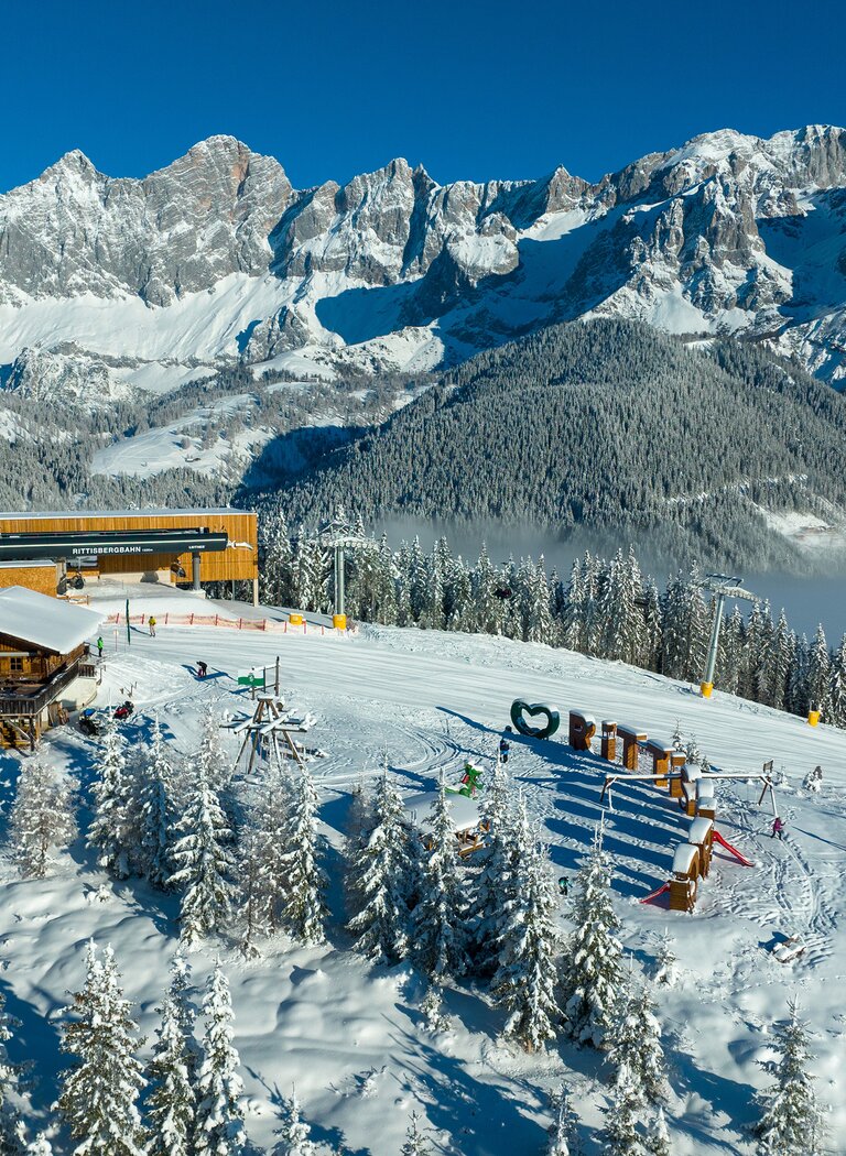 Verschneiter Rittisberg mit Rittisstadl, Bergstation, Winterspielplatz und imposantem Blick auf das Dachsteinmassiv. | © Rittis-Lift Engelhardt GmbH & Co KG