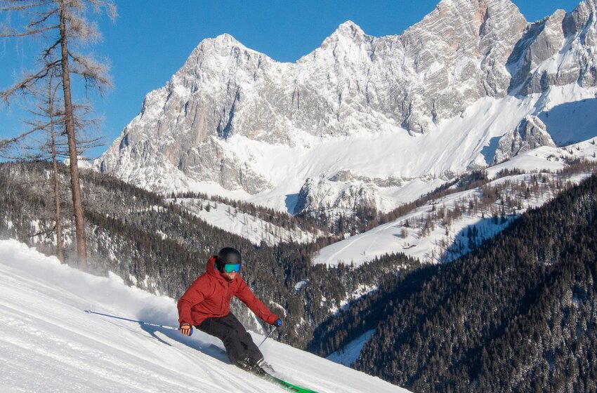 A skier descends a sunny slope at Rittisberg with snowy Dachstein mountains in the background. | © Rittis-Lift Engelhardt GmbH & Co KG