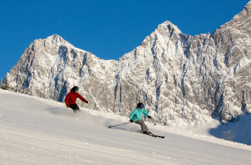 Two skiers descend a sunny slope at Rittisberg with an impressive view of the Dachstein south face. | © Rittis-Lift Engelhardt GmbH & Co KG