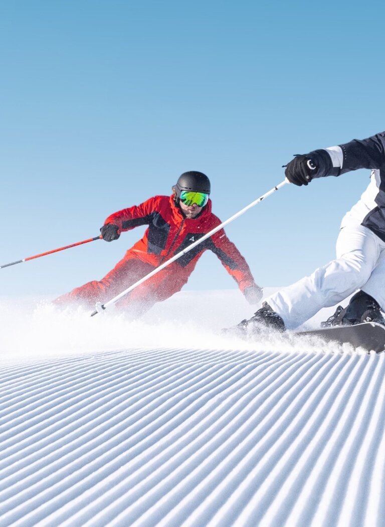 Zwei Skifahrer carven mit Tempo über frisch präparierte Piste | © Ski amadé GmbH Zwei Skifahrer in sportlicher Haltung fahren nebeneinander über frisch präparierte Rillenpiste bei Sonnenschein in Ski amadé. | © Ski amadé GmbH